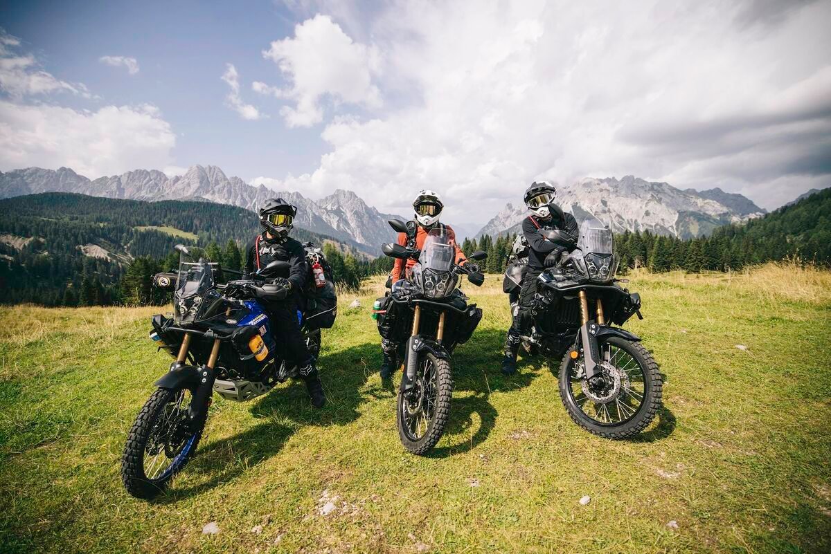 Three adventure motorcycle riders posing with mountain backdrop