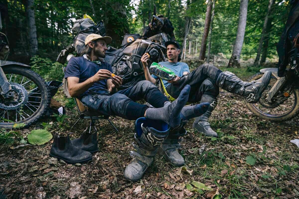 Two riders resting by their motorcycles in the forest